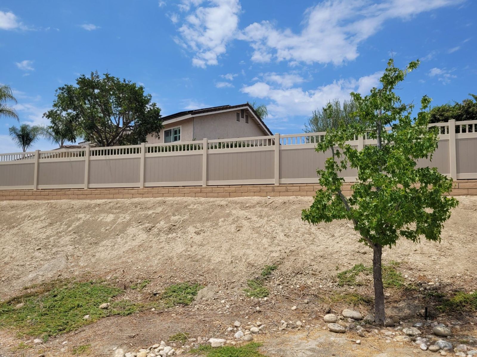 Tan vinyl privacy fence with picket top on a block wall