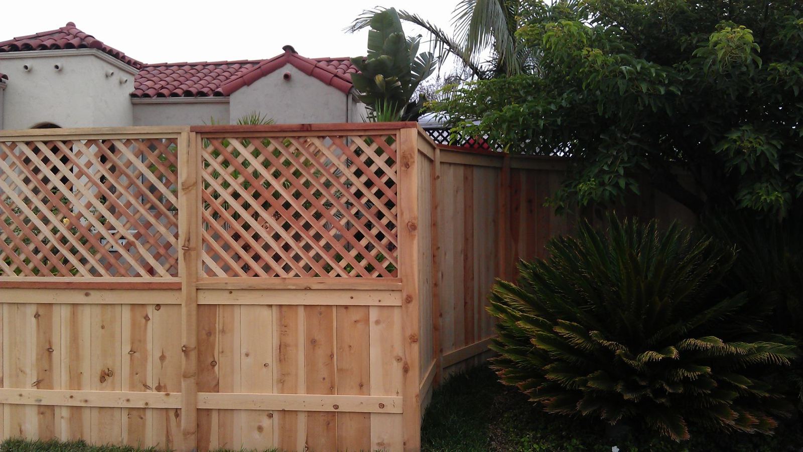 New cedar fence with lattice top and redwood-stained cap running around a corner